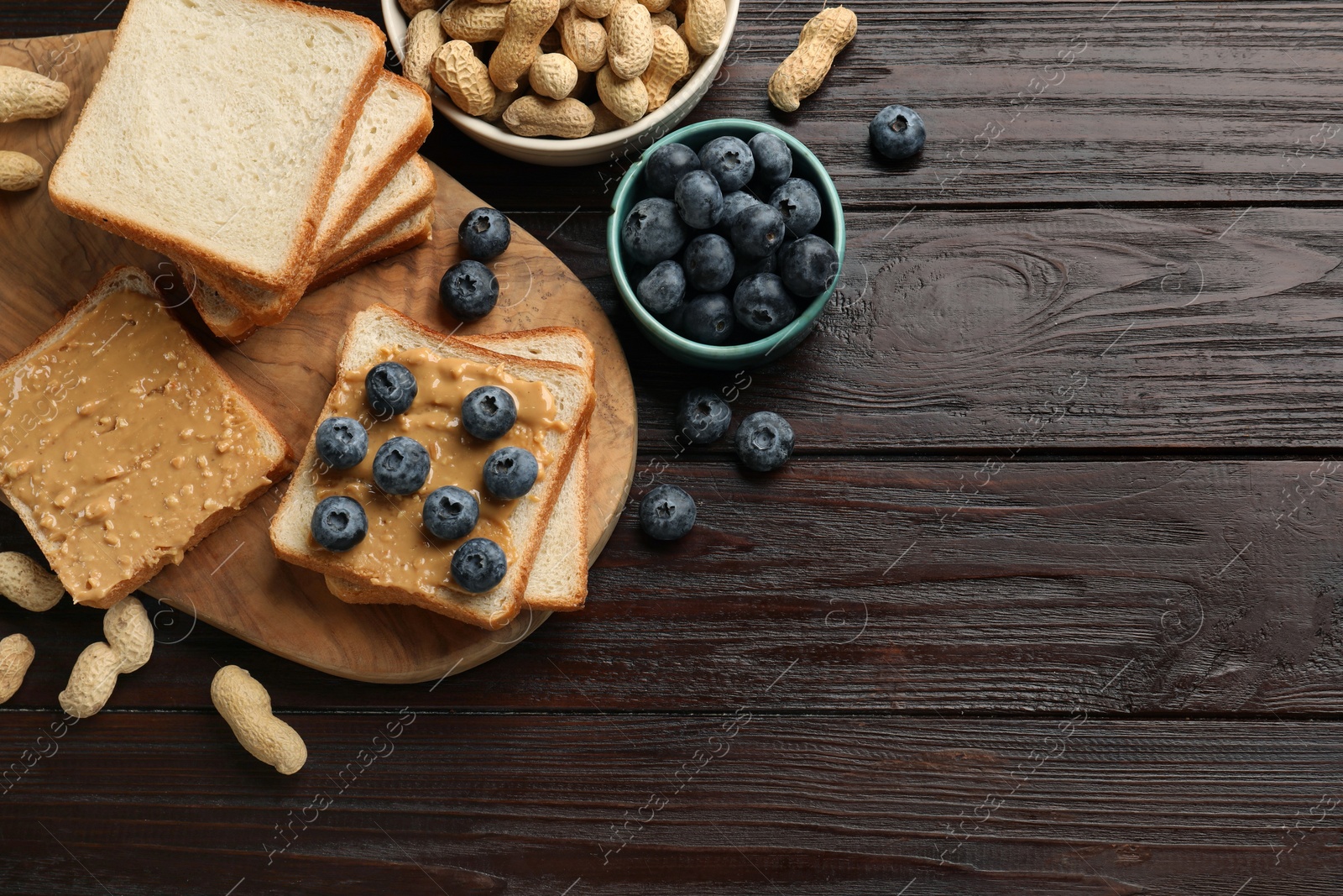 Photo of Delicious toasts with peanut butter, blueberries and nuts on wooden table, flat lay. Space for text