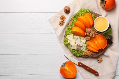 Photo of Delicious persimmon, blue cheese, nuts and honey served on white wooden table, flat lay. Space for text