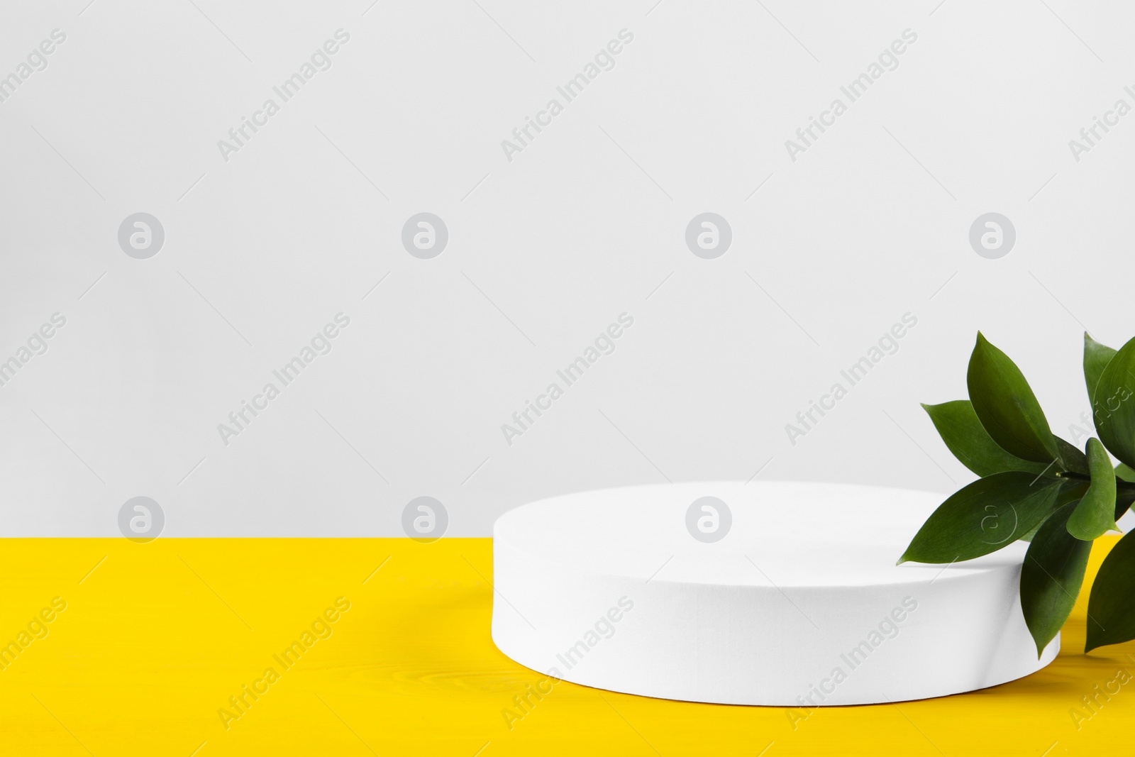 Photo of Green leaves and round shaped podium platform on yellow wooden table. Space for text