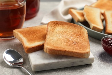 Photo of Slices of tasty toasted bread, jam and tea on light grey table
