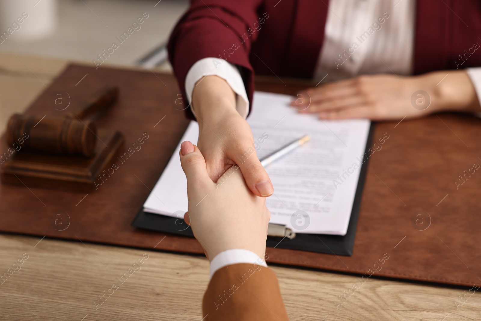 Photo of Notary shaking hands with client at wooden table in office, closeup