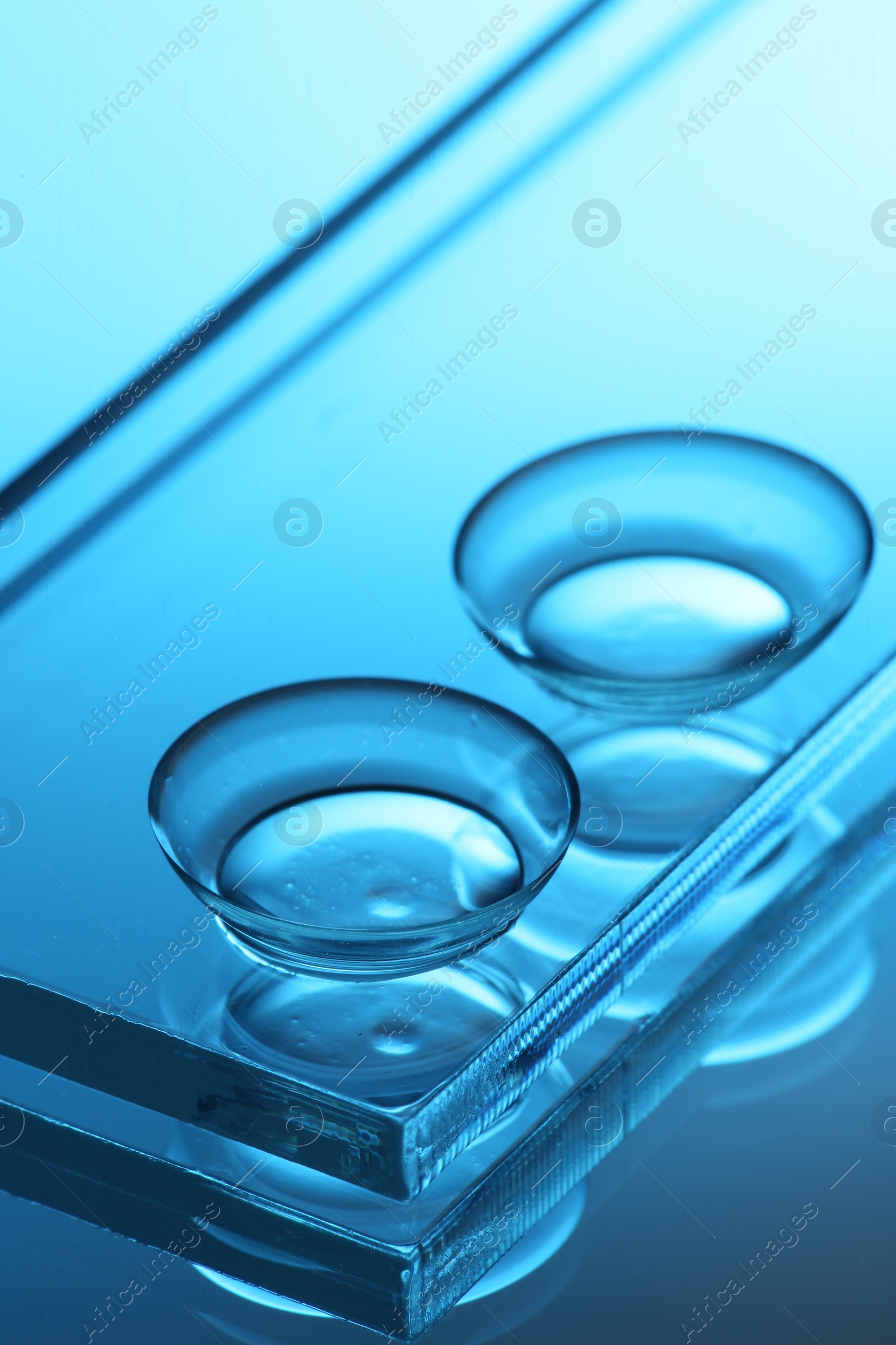 Photo of Pair of contact lenses and glass on mirror surface, closeup. Toned in blue