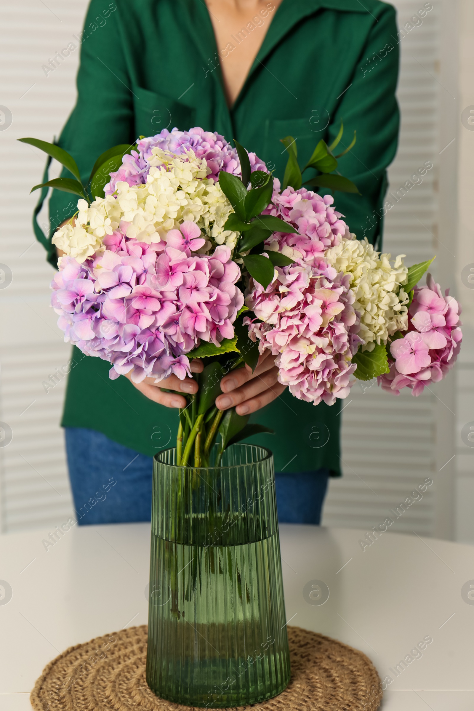 Photo of Woman with beautiful hydrangea flowers at table indoors, closeup. Interior design element