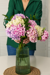 Woman with beautiful hydrangea flowers at table indoors, closeup. Interior design element