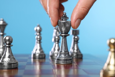 Man moving chess piece on checkerboard against light blue background, closeup