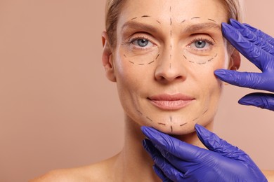 Photo of Doctor checking patient's face before cosmetic surgery operation on light brown background, closeup. Space for text