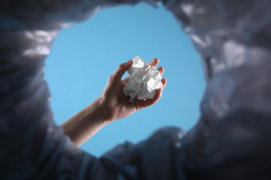 Photo of Bottom view of woman throwing crumpled paper into trash bin on light blue background, closeup