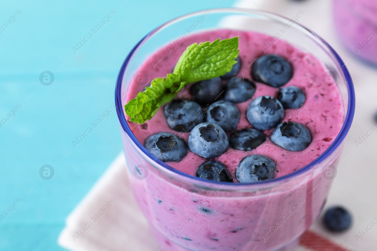 Photo of Glass of tasty blueberry smoothie with mint on light blue table, closeup