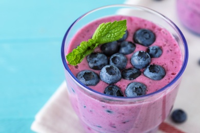 Photo of Glass of tasty blueberry smoothie with mint on light blue table, closeup