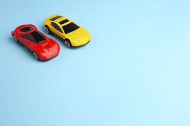 Photo of Two bright cars on light blue background, space for text. Children`s toys