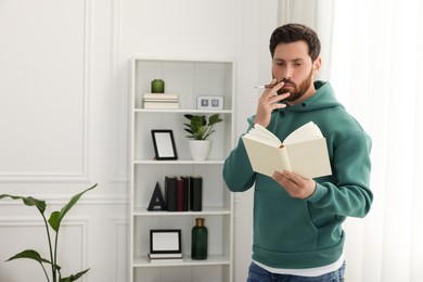 Photo of Man using cigarette holder for smoking white reading book indoors