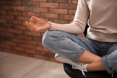 Photo of Woman meditating on chair near brick wall indoors, closeup