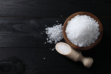 Photo of Organic salt in bowl and scoop on black wooden table, top view. Space for text