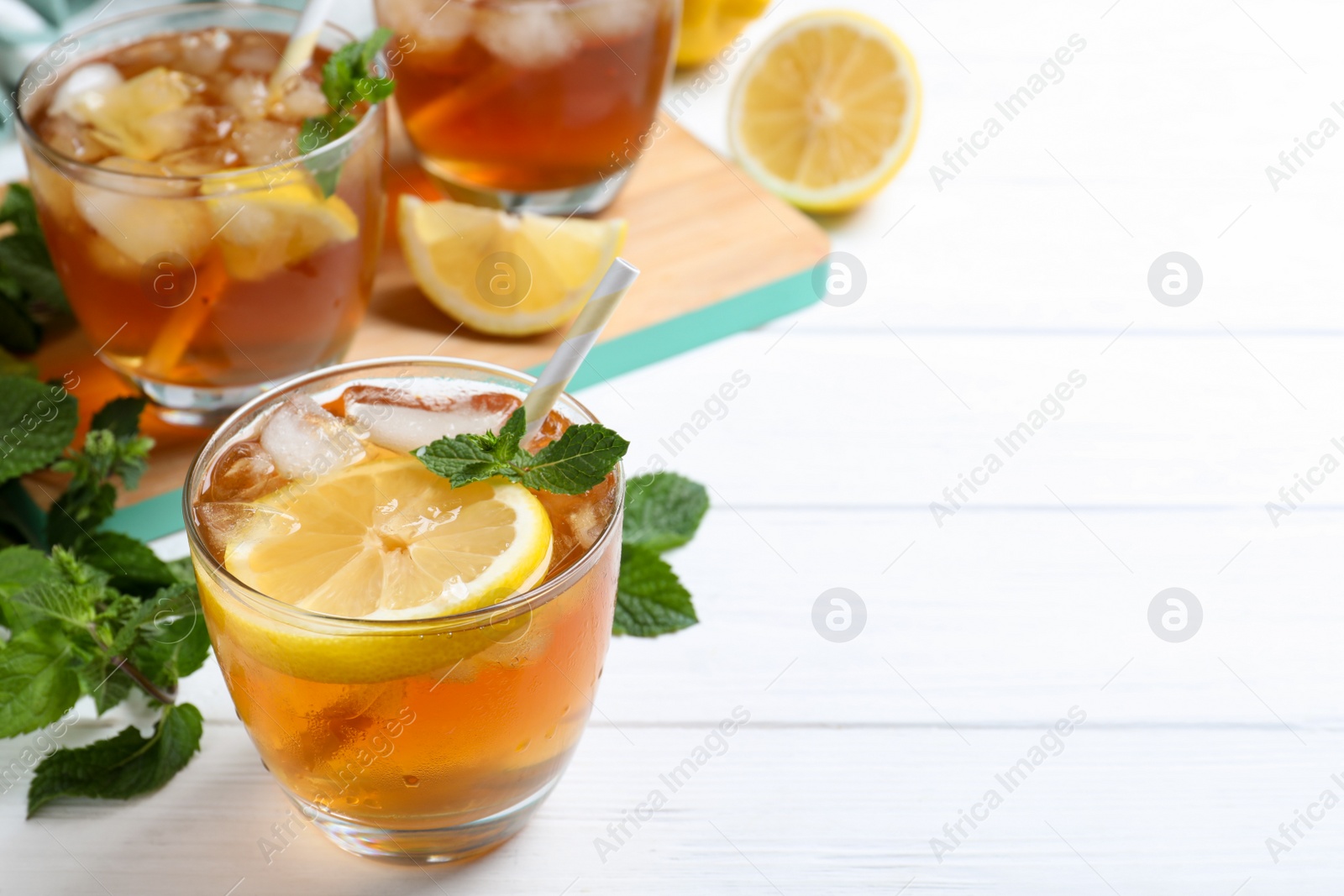 Photo of Delicious iced tea in glass on white wooden table, space for text