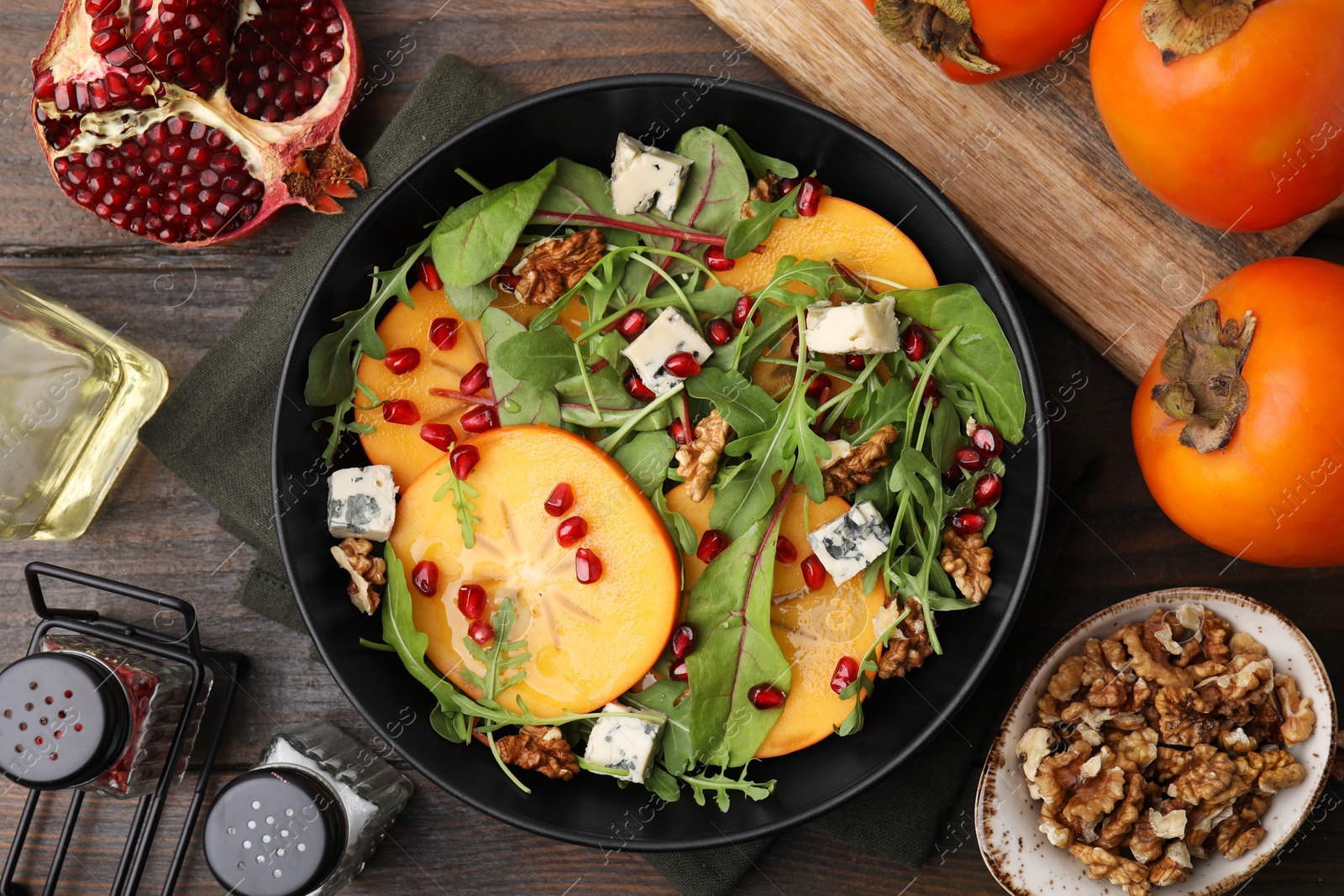 Photo of Tasty salad with persimmon, blue cheese, pomegranate and walnuts served on wooden table, flat lay