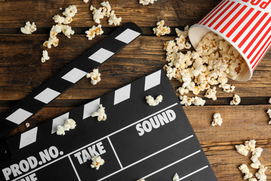 Photo of Tasty fresh pop corn and clapboard on wooden table, flat lay