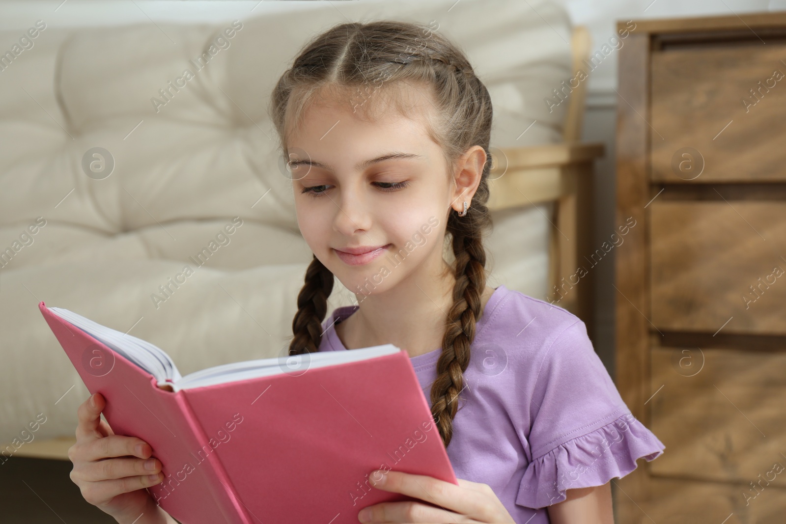 Photo of Cute little girl reading book at home