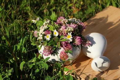 Photo of Ceramic mortar with pestle, different wildflowers and herbs on green grass outdoors