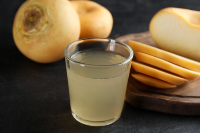 Photo of Glass of fresh natural turnip juice, cut and whole roots on black table