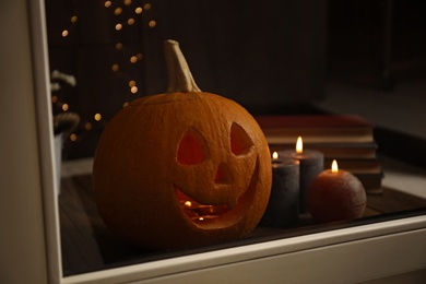 Composition with pumpkin head on windowsill, view through glass. Jack lantern - traditional Halloween decor