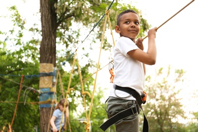 Photo of Little African-American boy climbing in adventure park. Summer camp