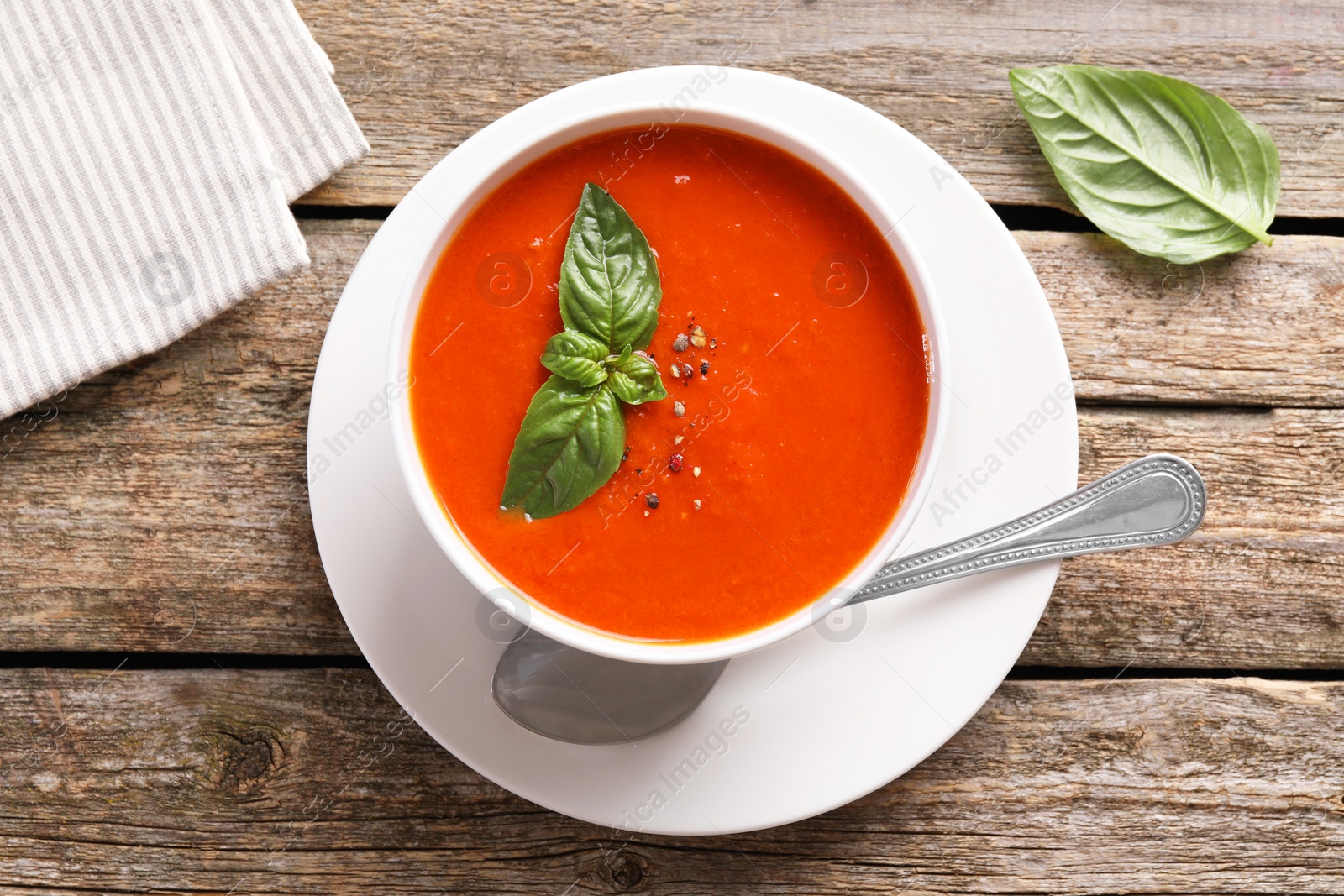 Photo of Delicious tomato soup with basil, spices and spoon on wooden table, flat lay