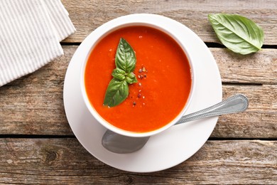 Photo of Delicious tomato soup with basil, spices and spoon on wooden table, flat lay