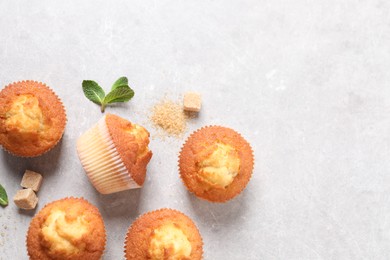 Delicious sweet muffins and brown sugar on light grey textured table, flat lay. Space for text