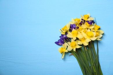 Bouquet of beautiful yellow daffodils and iris flowers on light blue wooden table, top view. Space for text