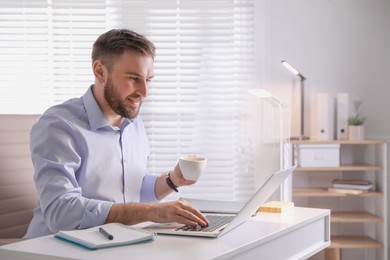 Photo of Young man with coffee working on laptop at table in office