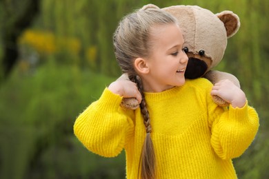 Photo of Cute little girl with teddy bear outdoors. Space for text