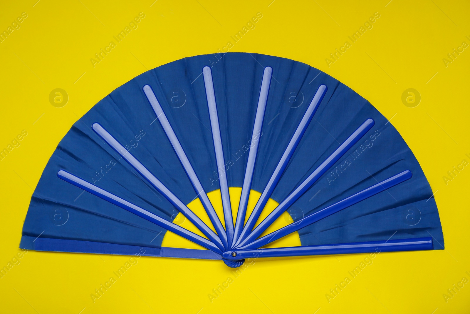 Photo of Bright blue hand fan on yellow background, top view