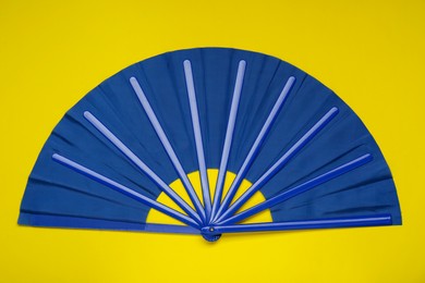 Photo of Bright blue hand fan on yellow background, top view