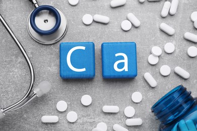 Photo of Light blue cubes with symbol Ca (Calcium), medical bottle and pills on gray background, top view