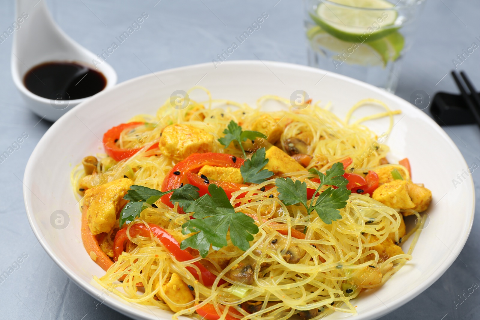 Photo of Stir-fry. Delicious cooked noodles with chicken and vegetables in bowl on gray table, closeup