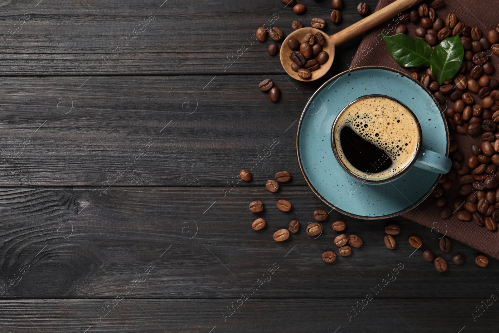Photo of Cup of aromatic hot coffee and beans on black wooden table, flat lay. Space for text