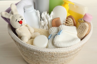 Photo of Wicker basket full of different baby cosmetic products, bathing accessories and toy on wooden table, closeup