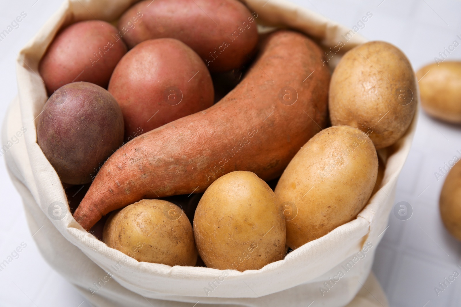 Photo of Different types of fresh potatoes in bag on white table, closeup
