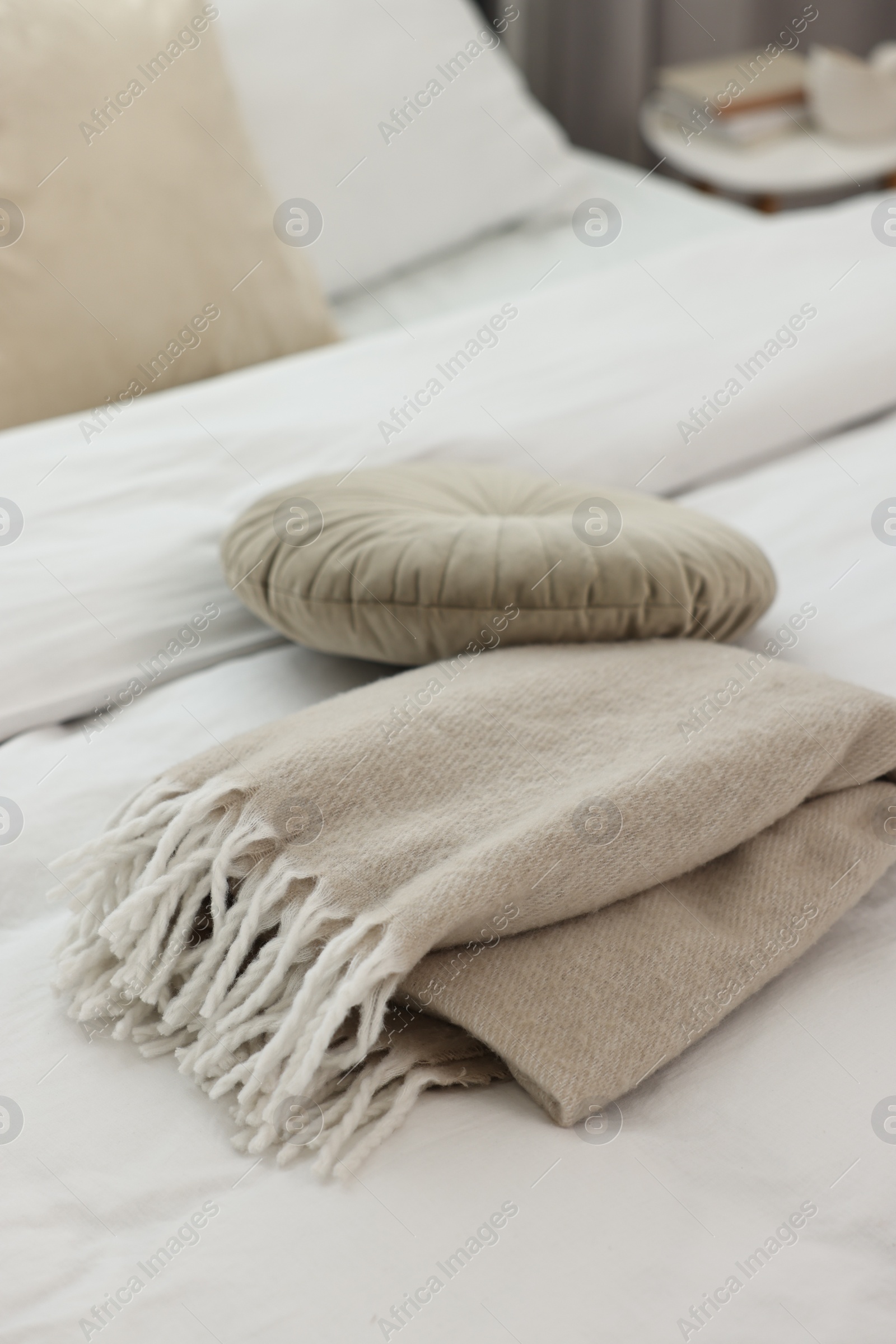 Photo of Soft beige plaid and pillow on bed in room