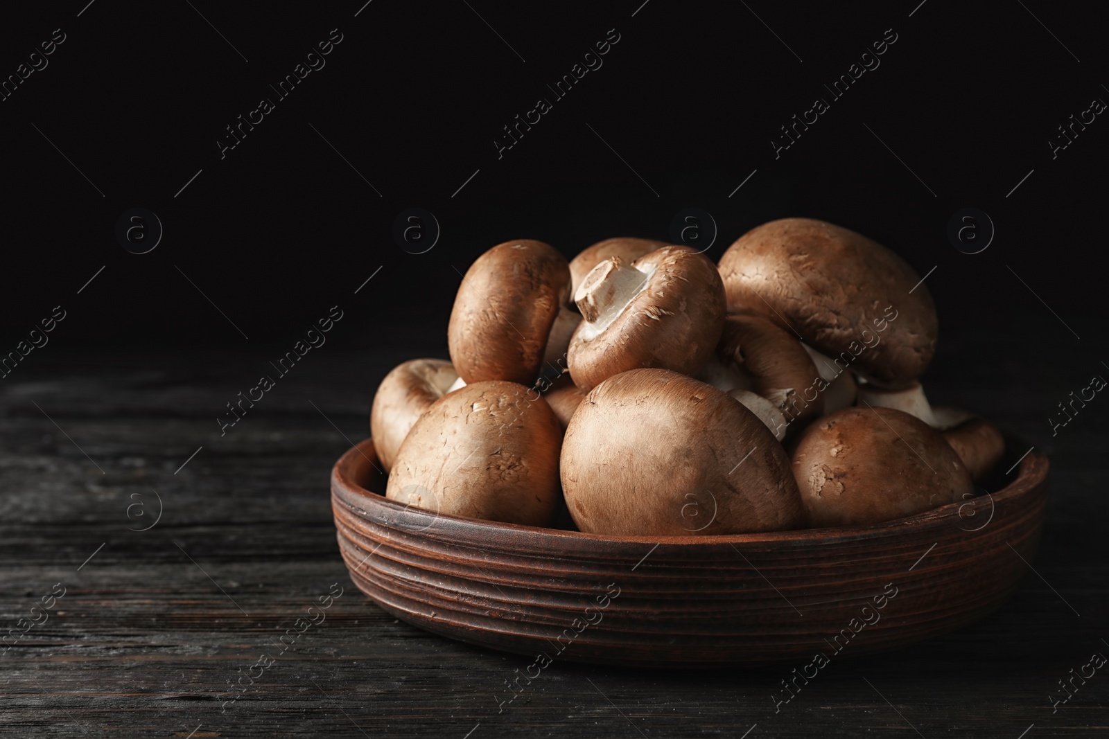 Photo of Bowl with fresh champignon mushrooms on wooden table. Space for text