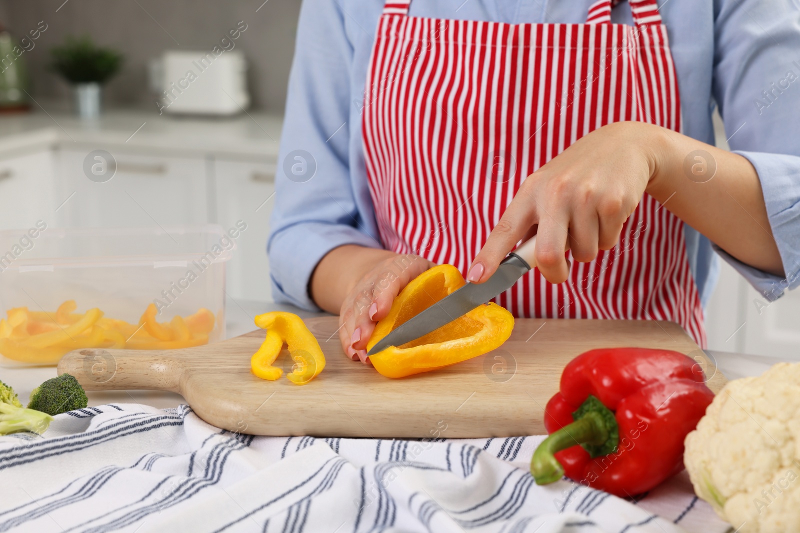 Photo of Woman cutting bell pepper near food storage container at table in kitchen, closeup
