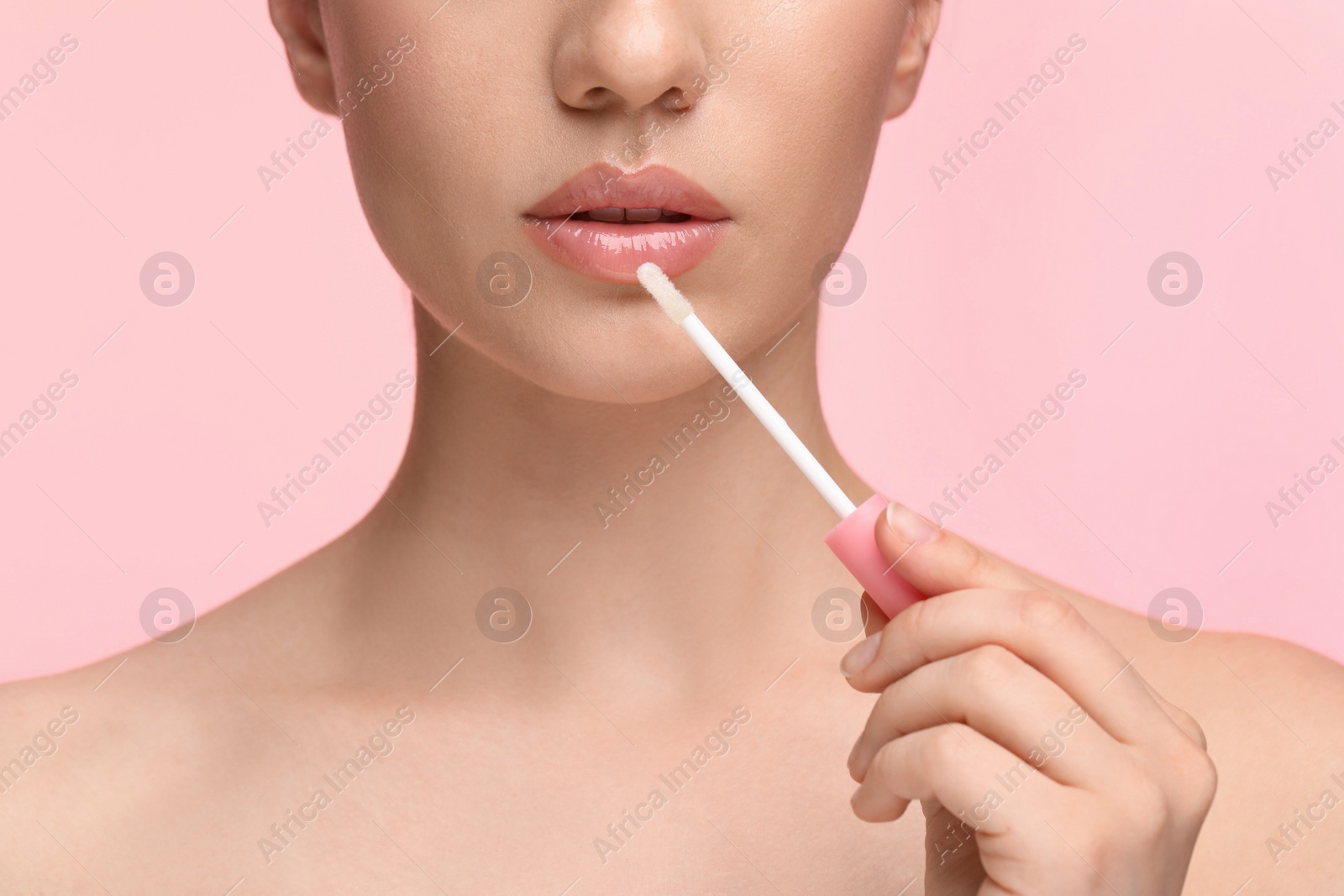 Photo of Woman applying lip gloss on pink background, closeup