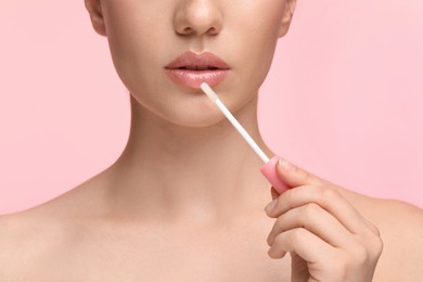 Woman applying lip gloss on pink background, closeup