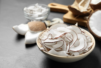 Photo of Tasty coconut chips in bowl on black table