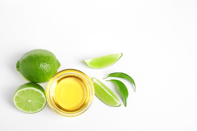 Photo of Lime essential oil in bowl and citrus fruits on white background, top view