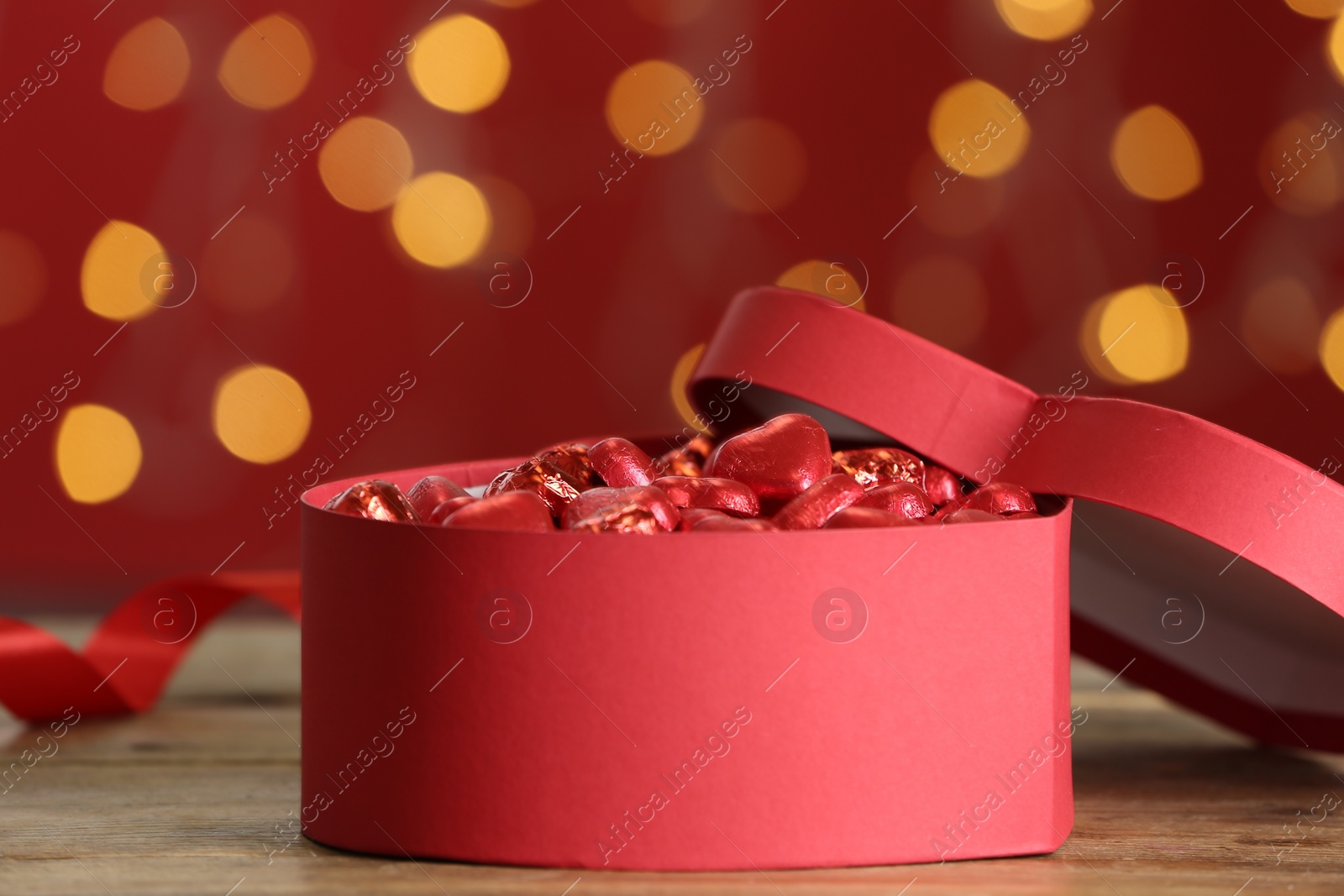 Photo of Heart shaped chocolate candies in gift box on table against blurred lights. Valentines's day celebration