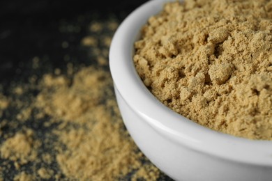 Photo of Bowl of mustard powder on black table, closeup. Space for text