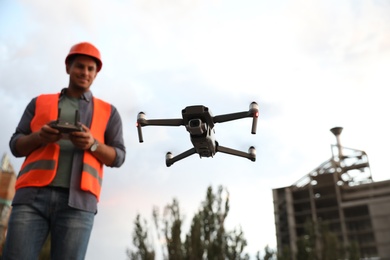 Builder operating drone with remote control at construction site, focus on quadcopter. Aerial survey