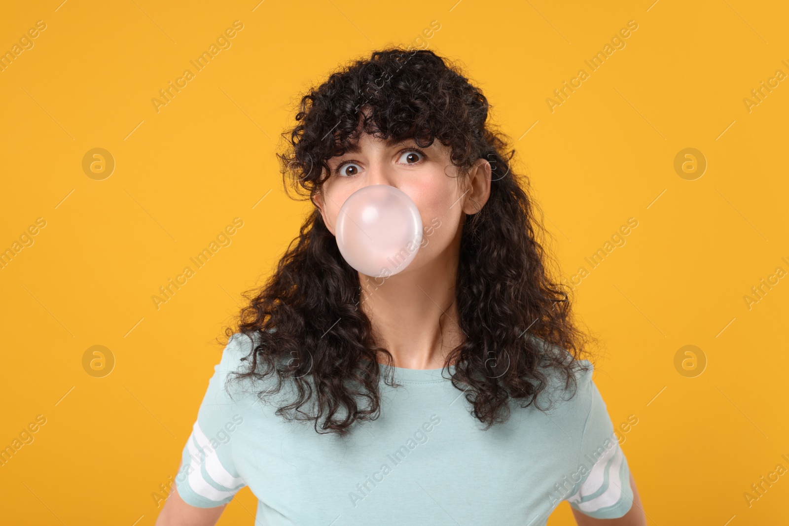 Photo of Beautiful young woman blowing bubble gum on orange background