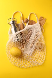 Photo of Fishnet bag with different items on yellow background, top view. Conscious consumption